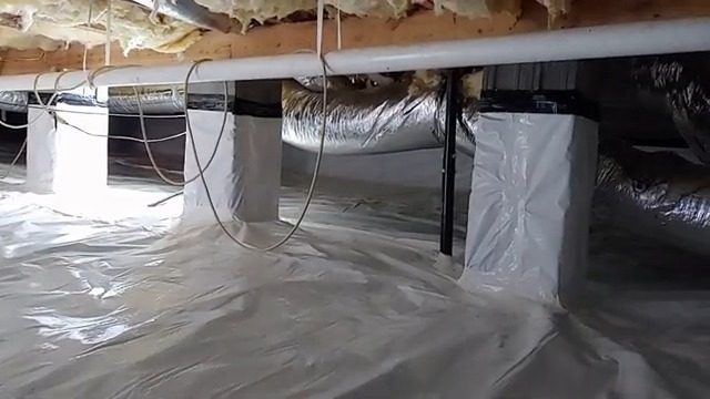Same crawl space after work: white vapor barrier covering the ground and wrapped piers