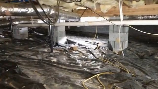 Crawl space before work: loose dark ground plastic and exposed, damaged insulation