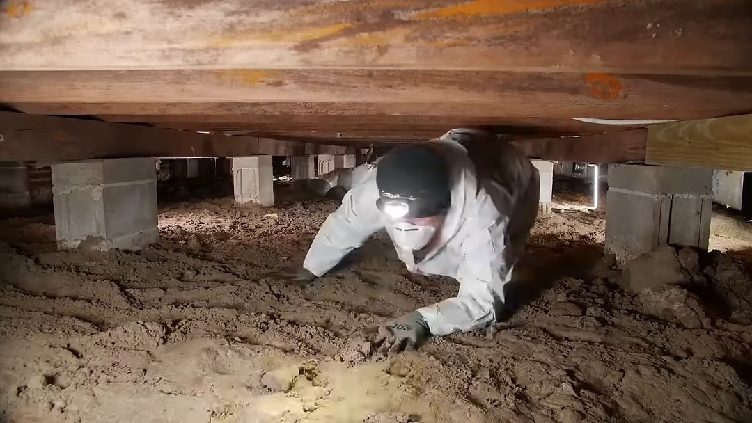 Technician inspecting the exposed dirt floor of a crawl space