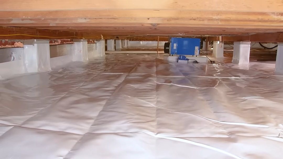 Crawl space with a white vapor barrier over the ground and a dehumidifier installed