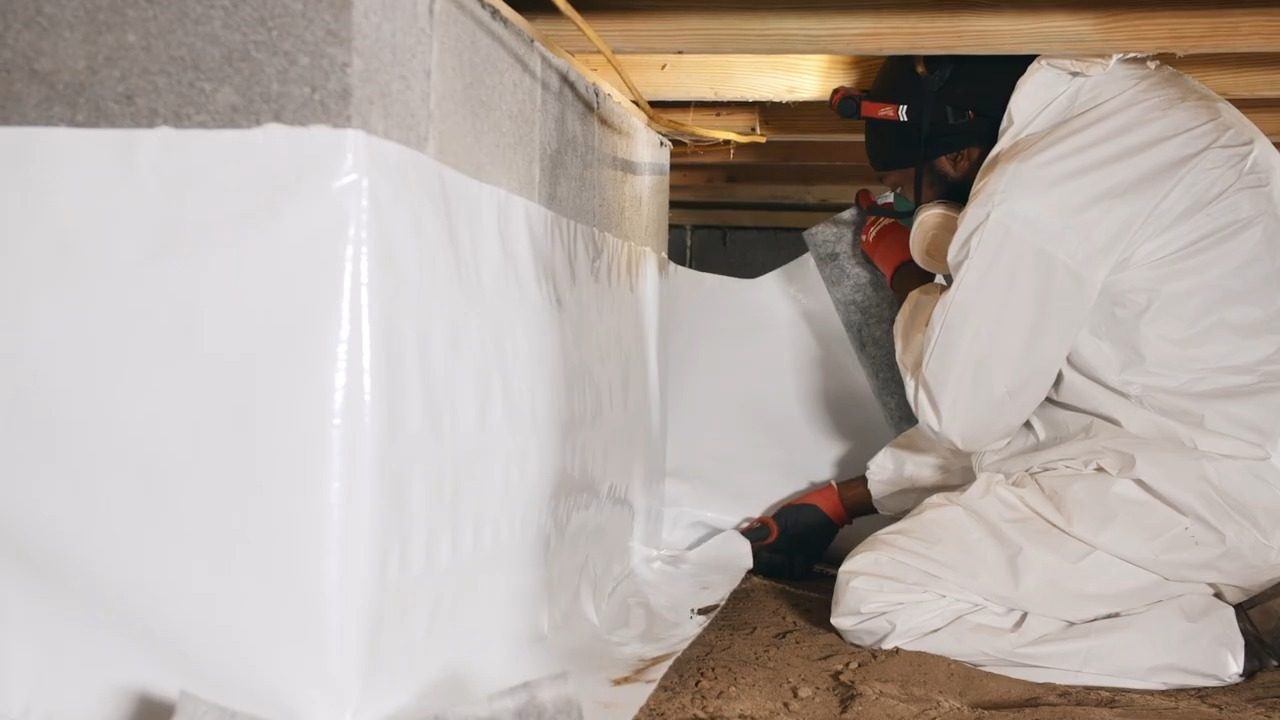 Technician fitting a vapor barrier liner on a crawl space wall